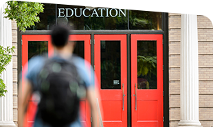 person walking toward the front red doors of the education building