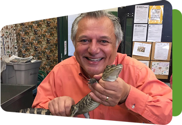 troy smiling at the camera in a classroom and holding a baby crocodile 