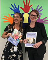 meg lopez and colleague holding wida booklets in front of colorful hand cut-outs