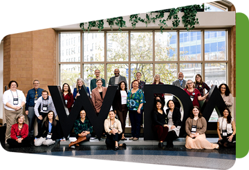 several wida staff posing around a large sculpture of the letters WIDA