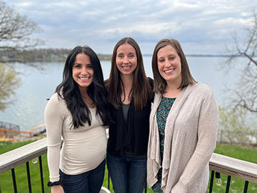 Three teachers posing in front of a lakeside background.