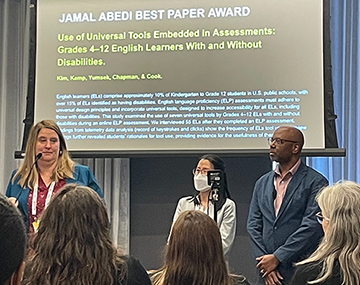 conference organizer and wida researchers in front of a screen that announces a best paper award