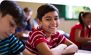 smiling boy at desk in classroom with other students