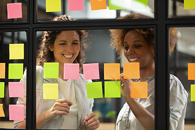 two women looking at post-it notes on glass window