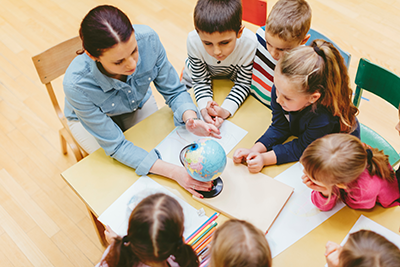 Teacher and students sitting around a table looking at a globe