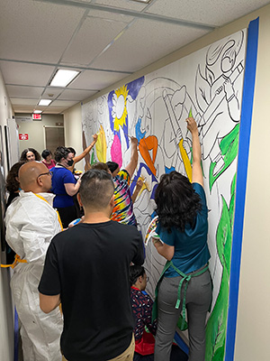 WIDA staff members painting mural on a wall in a hallway.