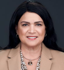 Headshot of Carmen wearing a beige coat and white printed top