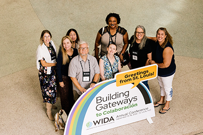 Group of educators stand in front of a 2026 WIDA Annual Conference sign that reads "Greetings from St. Louis."