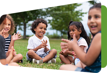 small group of young children sitting in the grass smiling and clapping